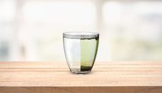 A glass with half purified water and half dirty water on a wooden table